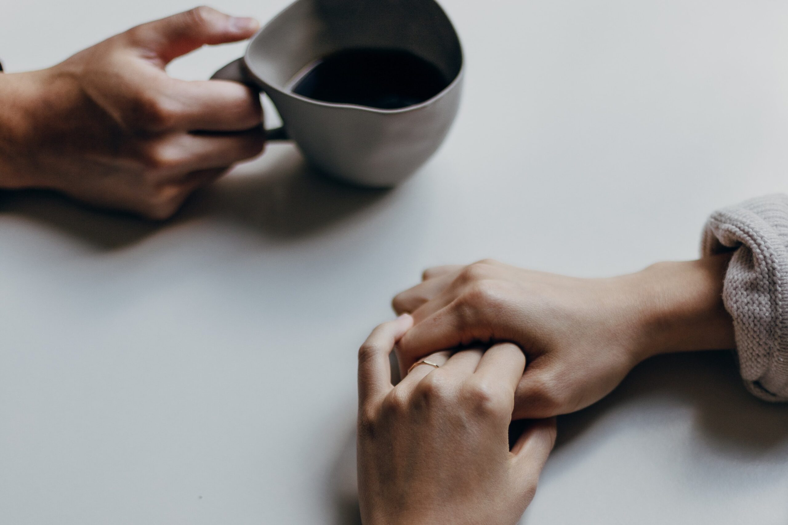 A hand holding a cup of coffee and another pair of hands nearby